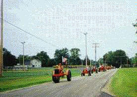 convoy of orange tractors drives down the road